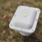 Small square seismic sensor mounted outdoors in grass, with a built-in spirit level visible on top.