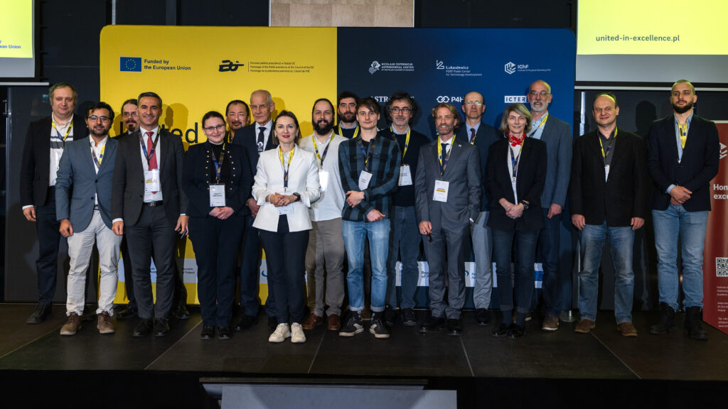 Group of people standing on a stage in front of a “United in Excellence” conference backdrop.