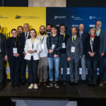 Group of people standing on a stage in front of a “United in Excellence” conference backdrop.
